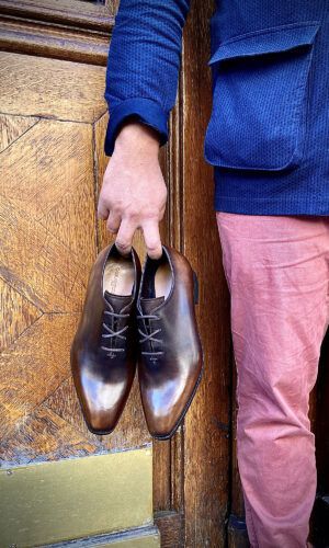 Un homme tient à la main une paire de richelieus one-cut patinés marrons.